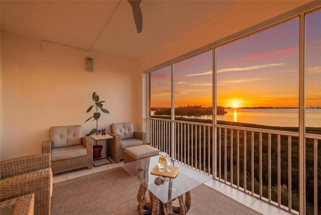 A screened-in balcony features wicker furniture and a glass coffee table overlooking a sunset view — 376 ARUBA CIRCLE UNIT 203, BRADENTON, FL
