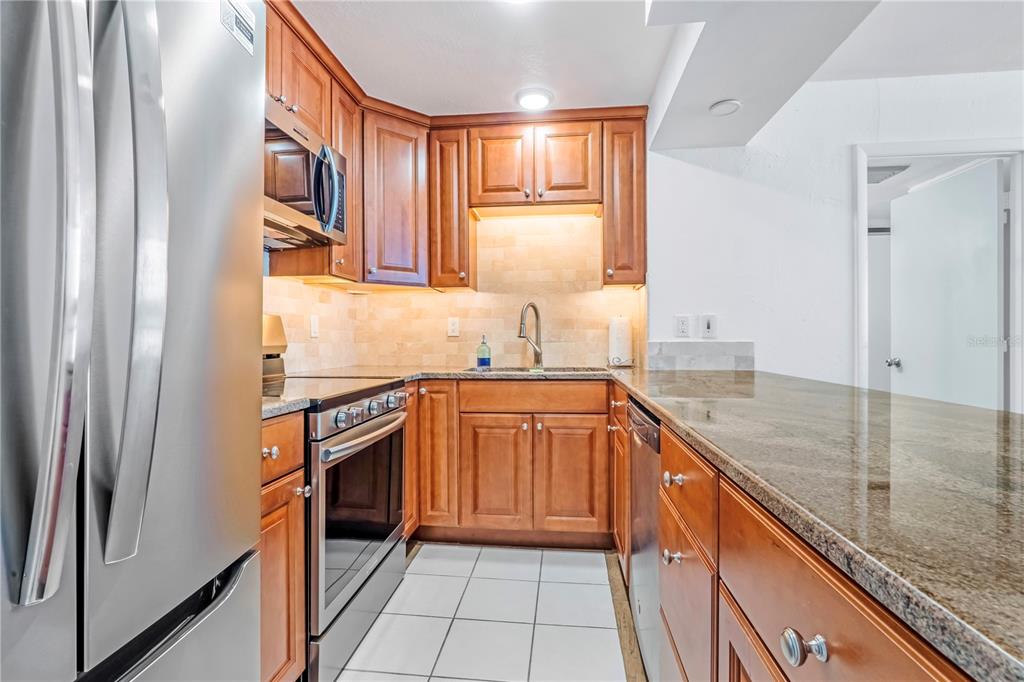 A kitchen features wood cabinets, granite countertops, stainless steel appliances, and white tile flooring — 3051 S ATLANTIC AVENUE UNIT 1705, DAYTONA BEACH SHORES, FL