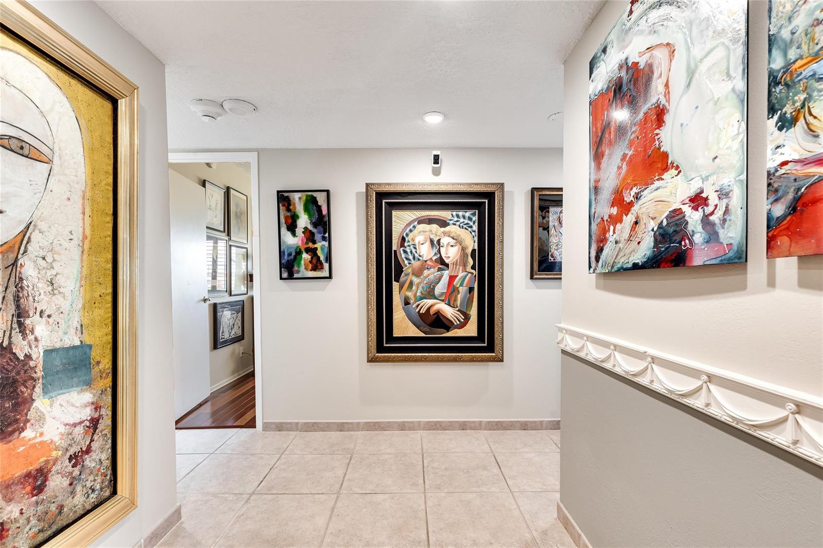 A hallway with tiled floors features multiple framed paintings displayed on the light-colored walls — 2500 E Las Olas Boulevard # 609, Fort Lauderdale FL 33301, FORT LAUDERDALE, FL