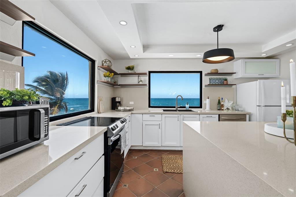 A white kitchen with quartz countertops, stainless steel appliances, and two windows overlooking the ocean — 91 G KENNEDY STREET, DORADO, PR