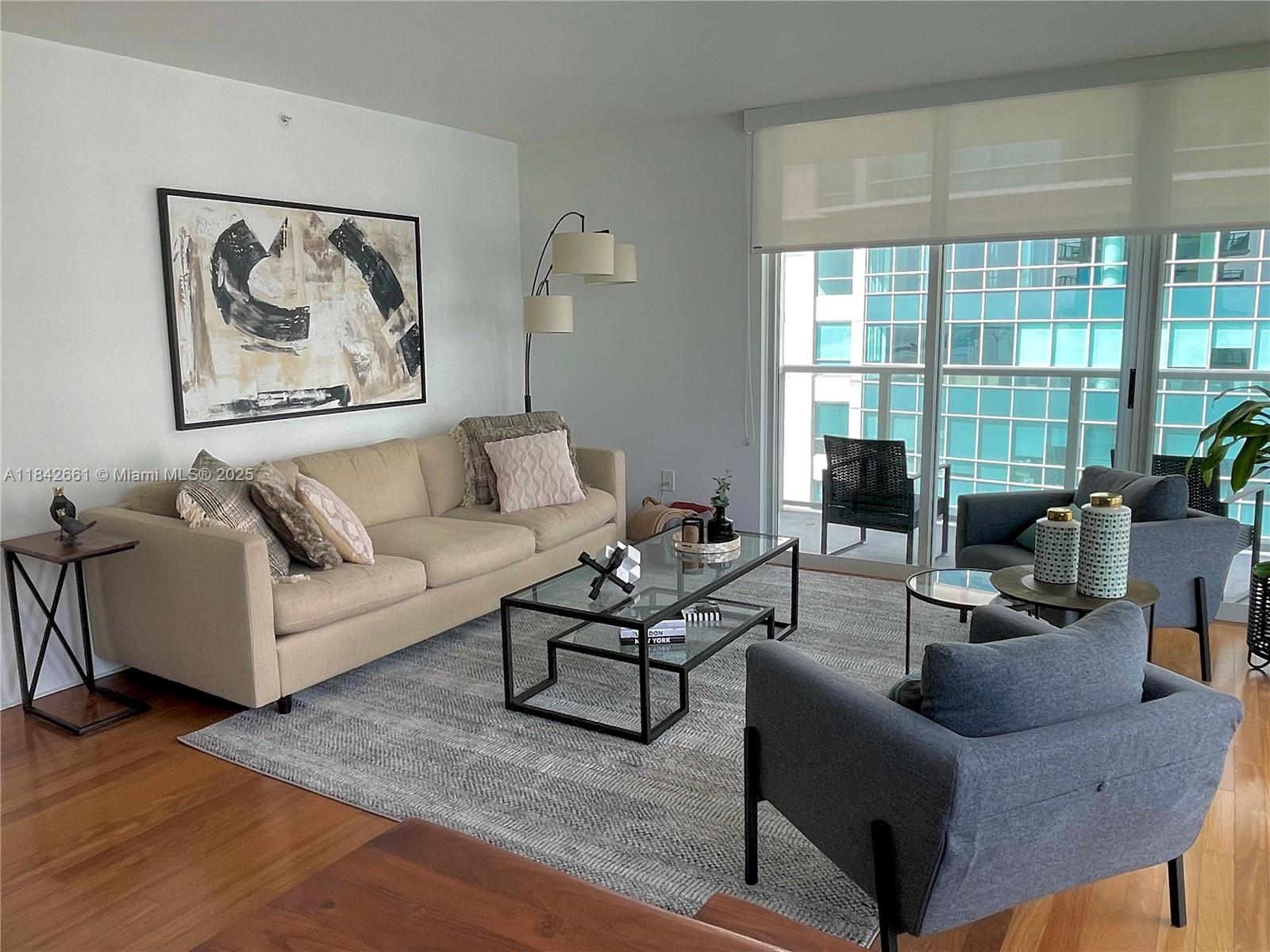 A living room features a beige sofa, two gray armchairs, a glass coffee table, and balcony access — 1155 Brickell Bay Dr # 2802, Miami FL 33131, MIAMI, FL
