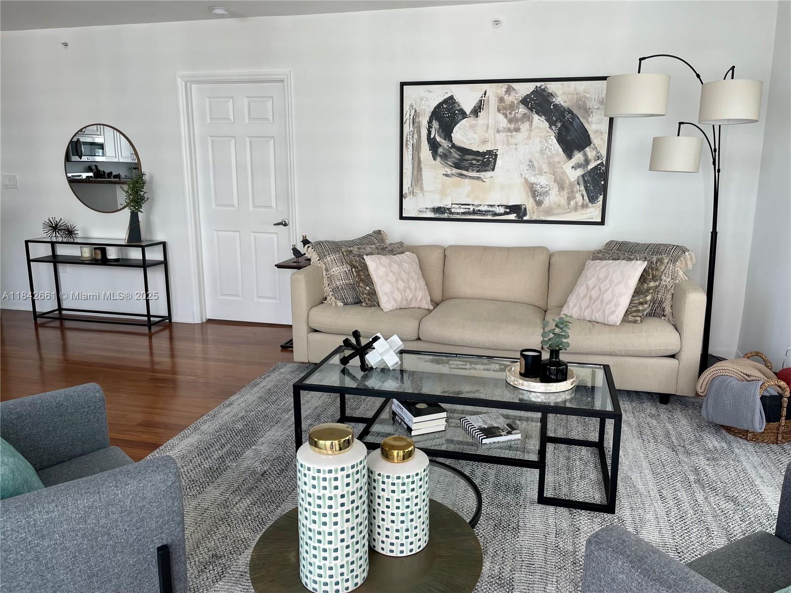 A living room features a beige sofa, glass coffee table, and abstract wall art — 1155 Brickell Bay Dr # 2802, Miami FL 33131, MIAMI, FL