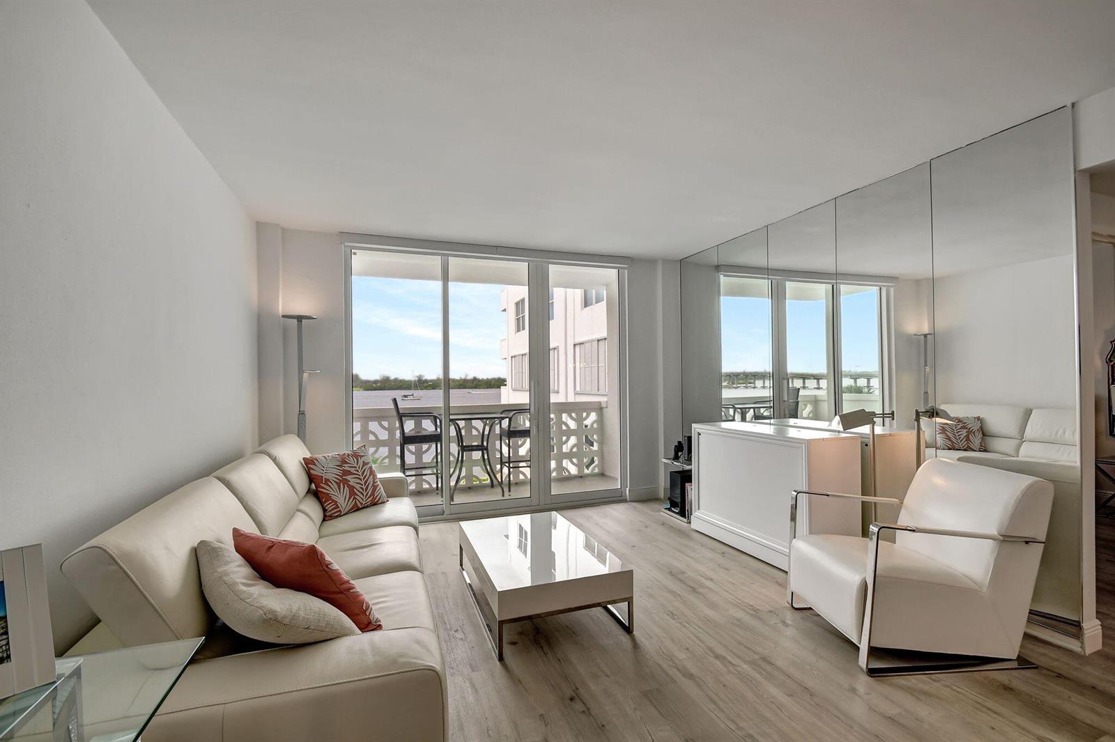 A living room with light wood floors, white leather furniture, and a mirrored accent wall — 2840 S Ocean Boulevard # 3020, Palm Beach FL 33480, PALM BEACH, FL