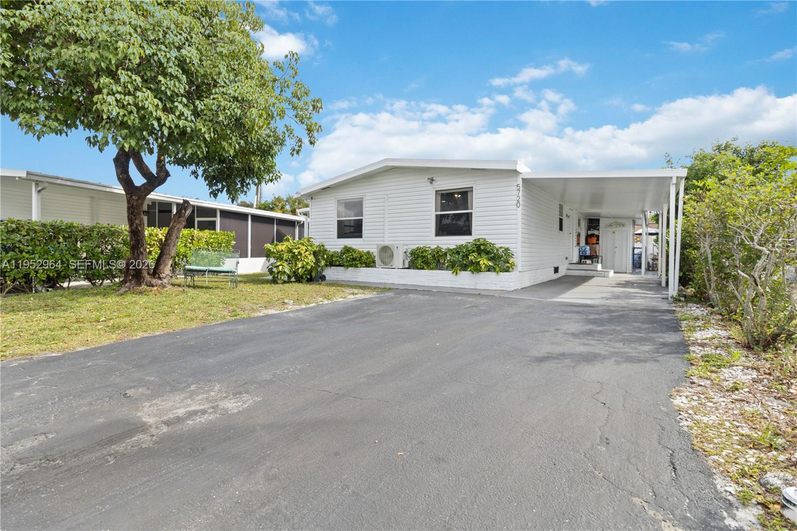 A white single-story manufactured home features a paved driveway, a carport, and a large tree — 5720 SW Cypress Dr, Dania Beach FL 33312, DANIA BEACH, FL