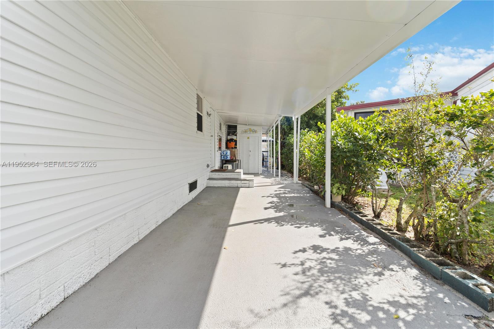 A covered concrete carport runs alongside the white siding of a mobile home — 5720 SW Cypress Dr, Dania Beach FL 33312, DANIA BEACH, FL