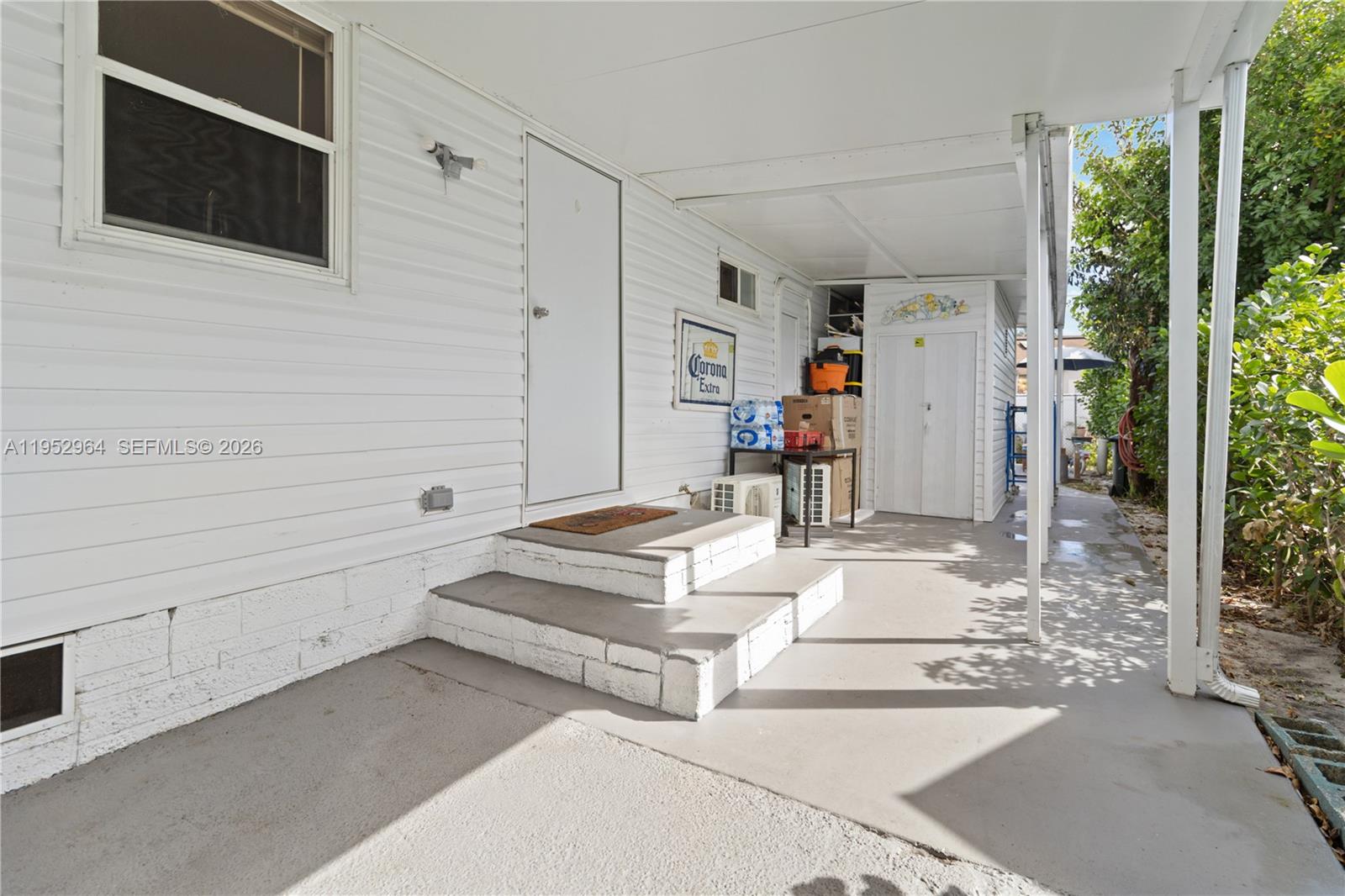 A white mobile home exterior features a covered patio, concrete steps, and a storage shed — 5720 SW Cypress Dr, Dania Beach FL 33312, DANIA BEACH, FL