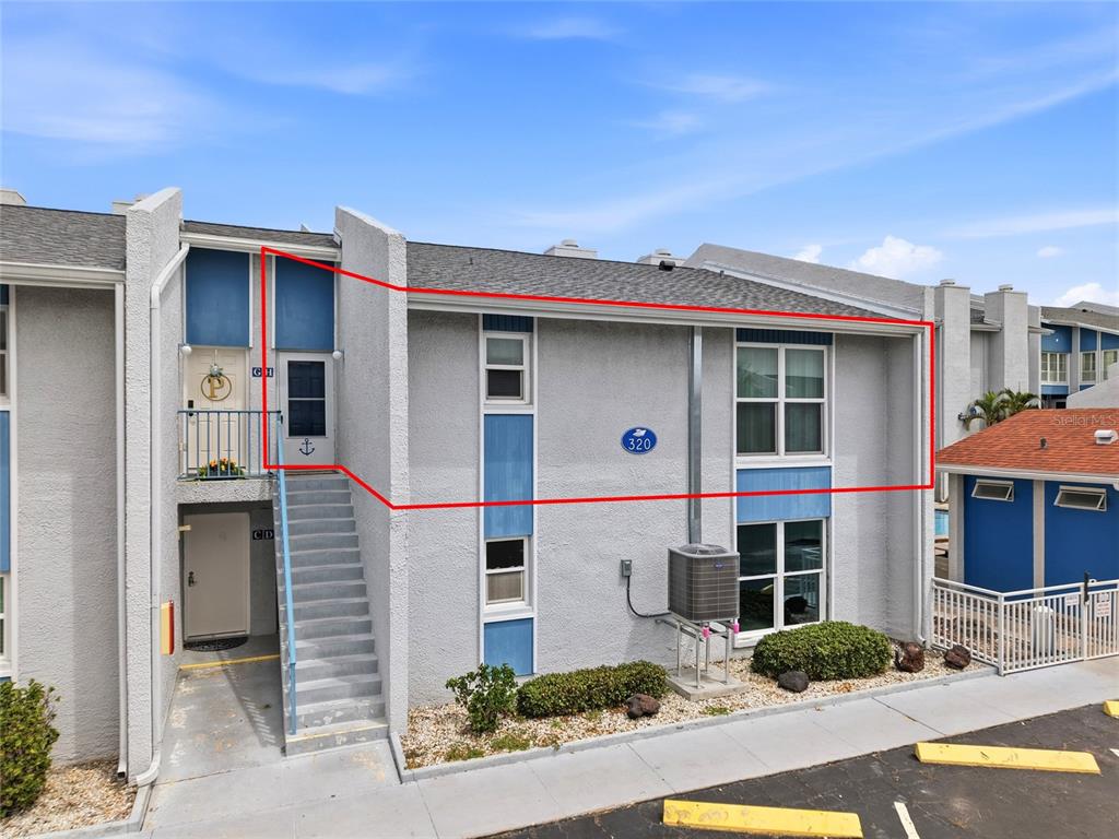 The exterior of a two-story residential building features gray stucco walls, blue accents, and stairs — 320 MEDALLION BOULEVARD UNIT H, MADEIRA BEACH, FL