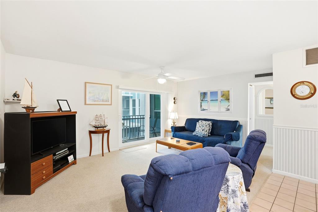 A living room features blue furniture, a television console, and a sliding glass balcony door — 320 MEDALLION BOULEVARD UNIT H, MADEIRA BEACH, FL