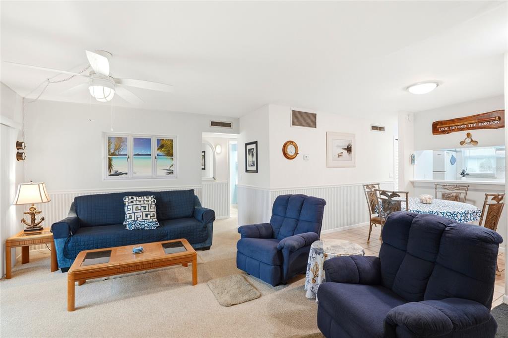 A living room with blue furniture, beige carpeting, and a dining area in the background — 320 MEDALLION BOULEVARD UNIT H, MADEIRA BEACH, FL
