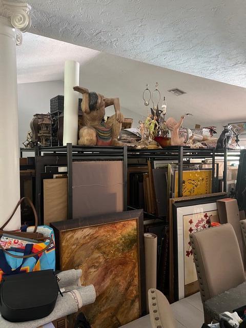 A room contains metal shelving units packed with various framed artwork, sculptures, and decorative items — Wellington Trace, Wellington FL, WELLINGTON, FL