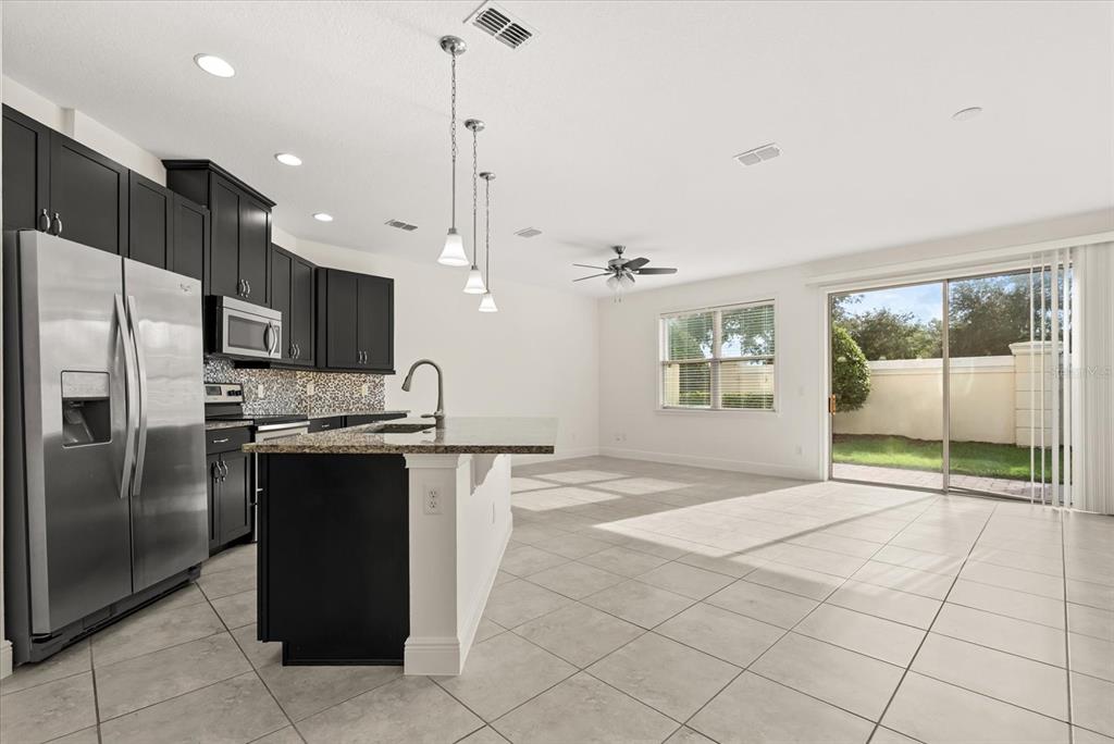 A kitchen with dark cabinets, granite countertops, and stainless steel appliances opens to a living area — 9829 WINNINGTON STREET, ORLANDO, FL