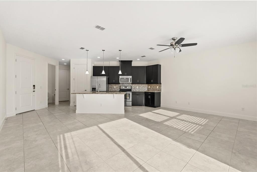 An open-concept kitchen features dark cabinets, a white island, and light tile flooring — 9829 WINNINGTON STREET, ORLANDO, FL