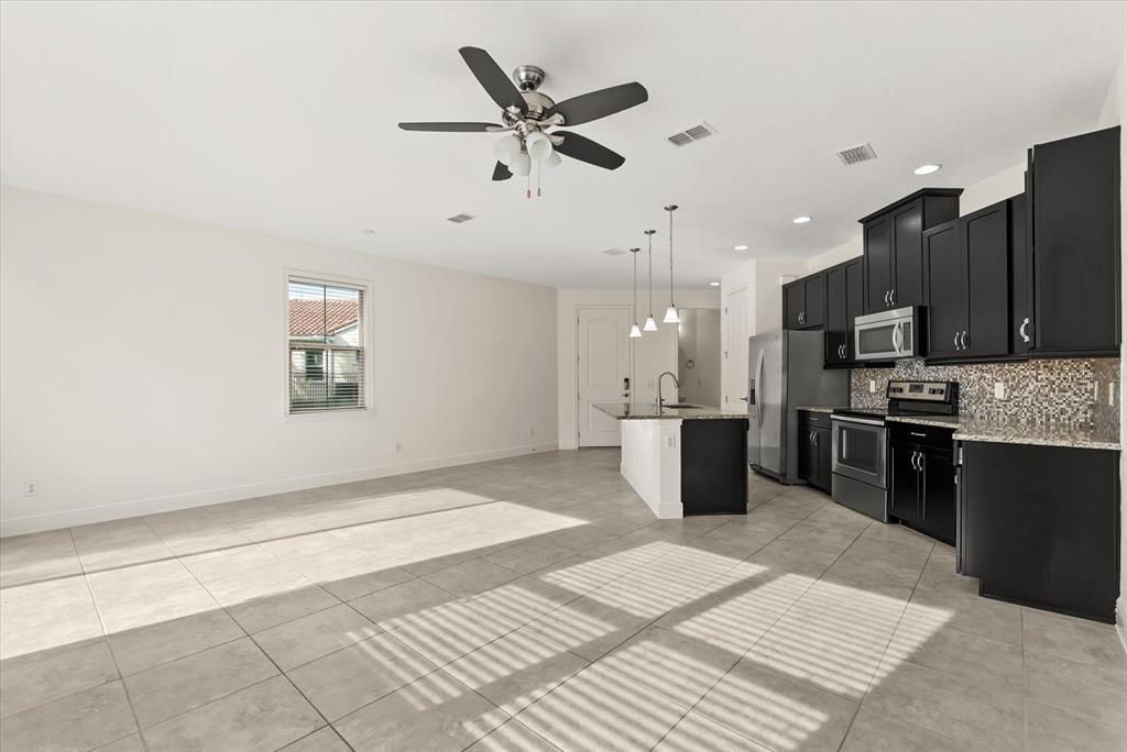 An open-concept kitchen and living area features tile flooring, black cabinetry, and a ceiling fan — 9829 WINNINGTON STREET, ORLANDO, FL