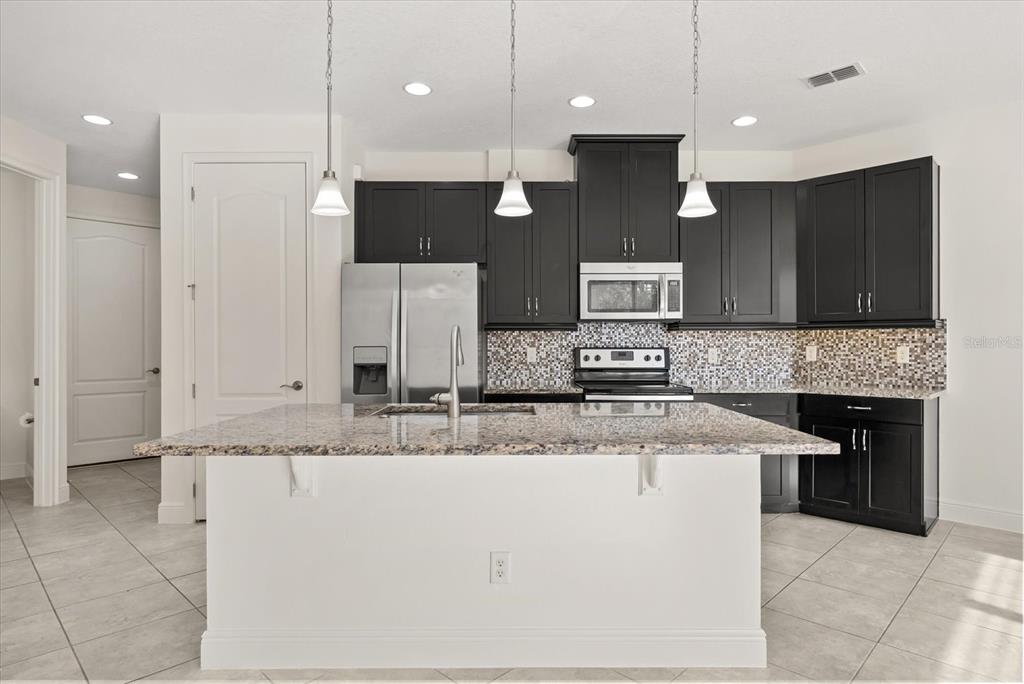 A kitchen features dark cabinets, granite countertops, a central island, and stainless steel appliances — 9829 WINNINGTON STREET, ORLANDO, FL