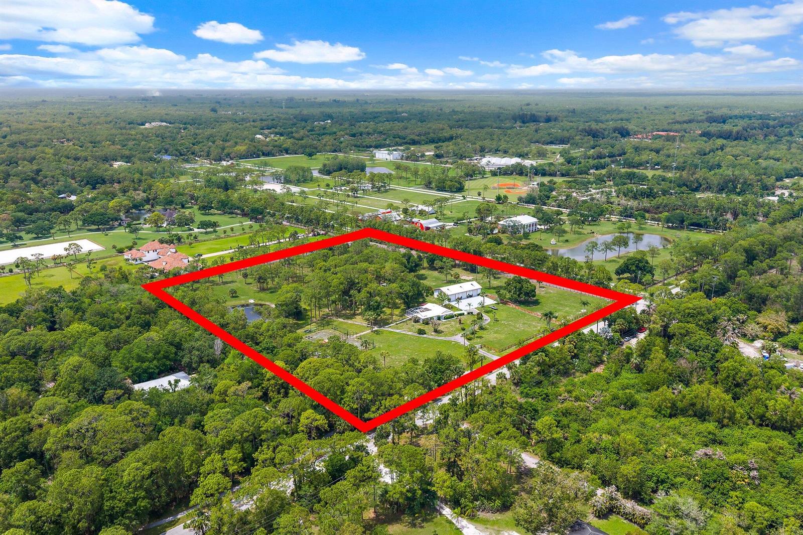 An aerial view shows a large, rectangular property with a house and barn surrounded by trees — 16411 Jupiter Farms Road, Jupiter FL 33478, JUPITER, FL