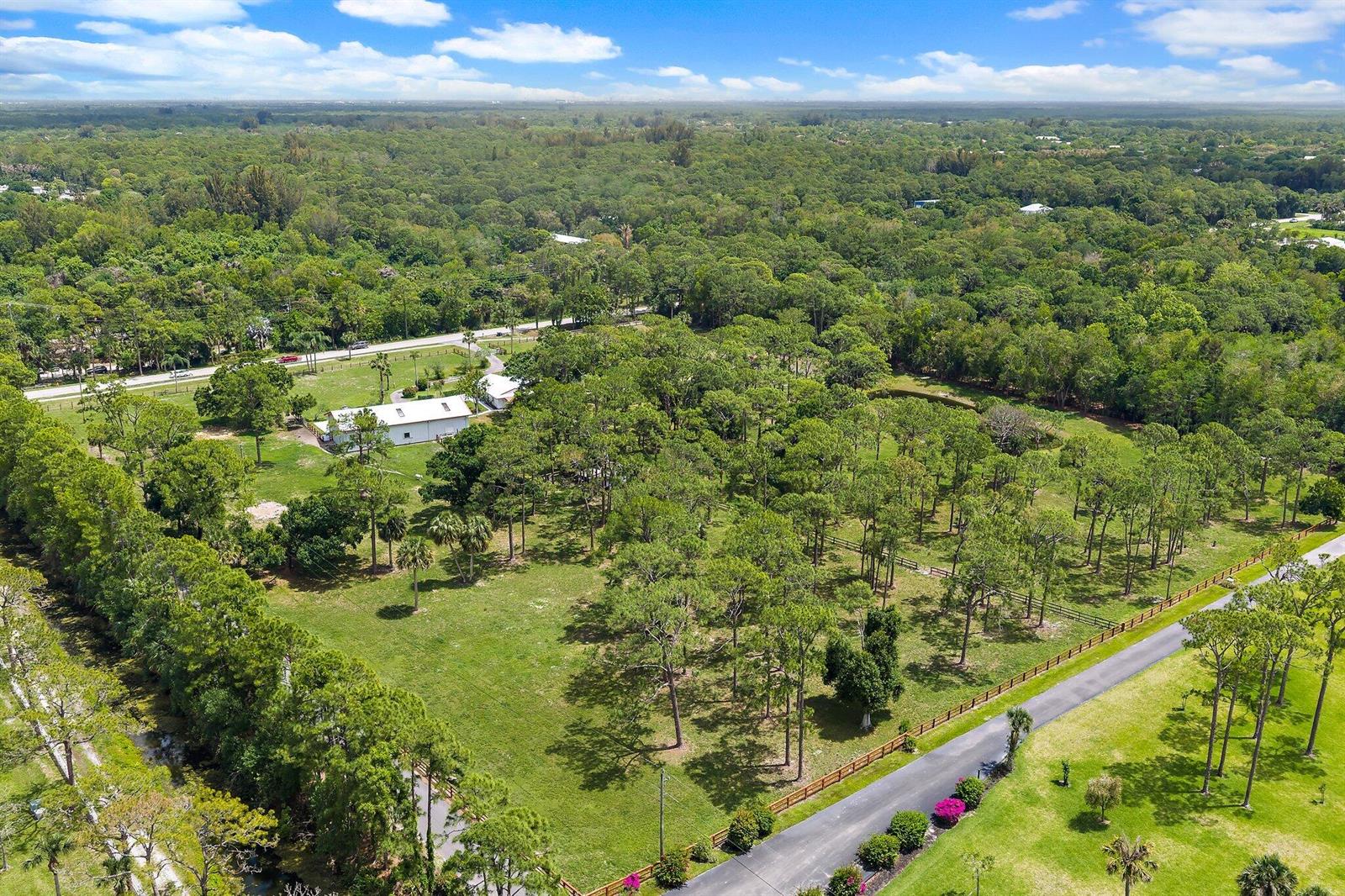 An aerial view shows a white house situated on a large, tree-filled rural property — 16411 Jupiter Farms Road, Jupiter FL 33478, JUPITER, FL
