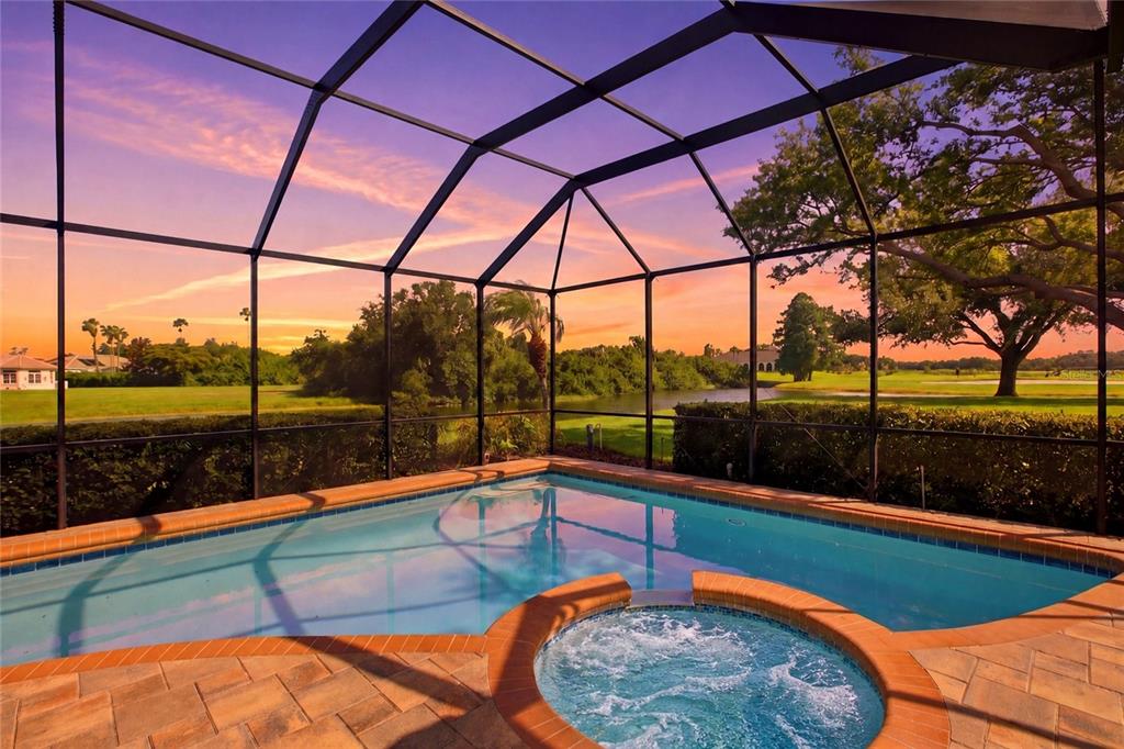 A screened-in swimming pool and hot tub overlook a golf course at sunset — 8417 LONE EAGLE WAY, SARASOTA, FL