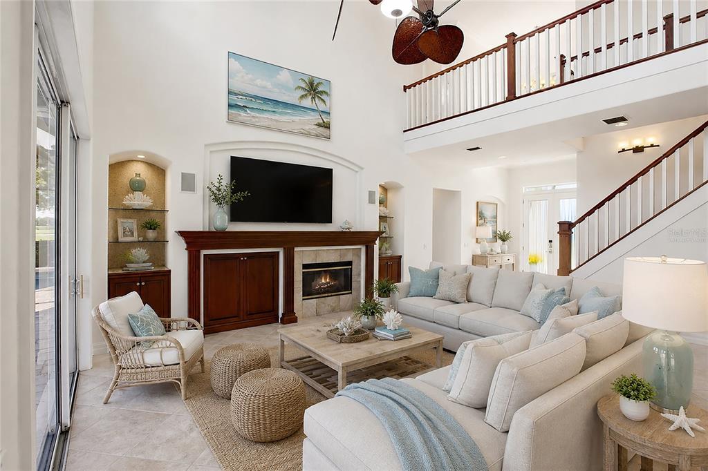 A bright living room features a fireplace, built-in shelving, and a balcony overlooking the space — 8417 LONE EAGLE WAY, SARASOTA, FL