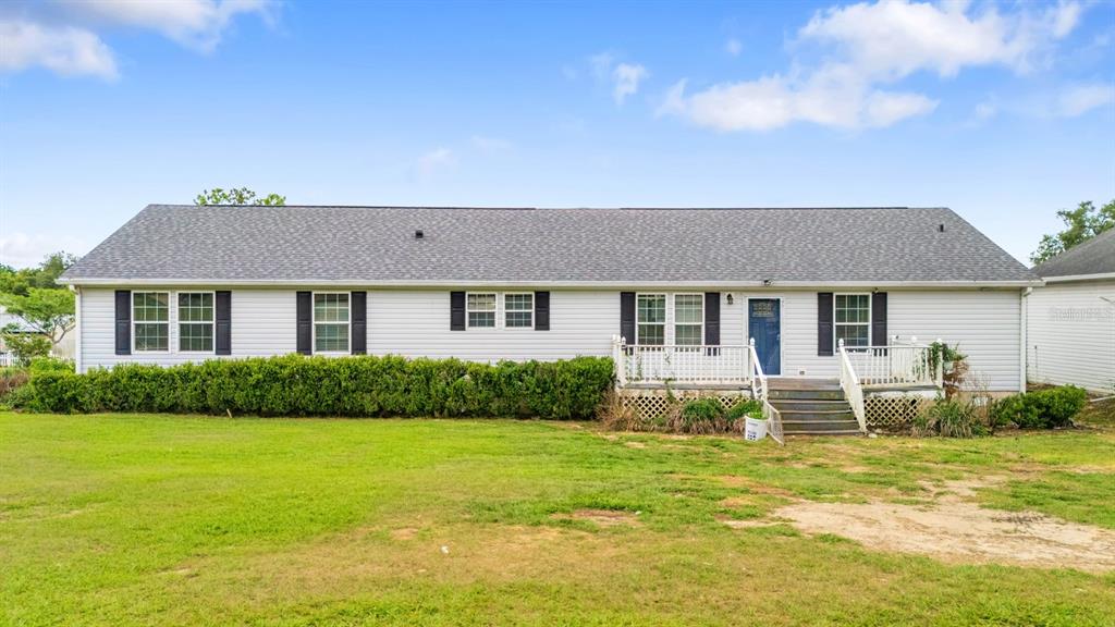 A single-story house with light siding, dark shutters, a gray roof, and a wooden deck — 37520 PHELPS ROAD, ZEPHYRHILLS, FL