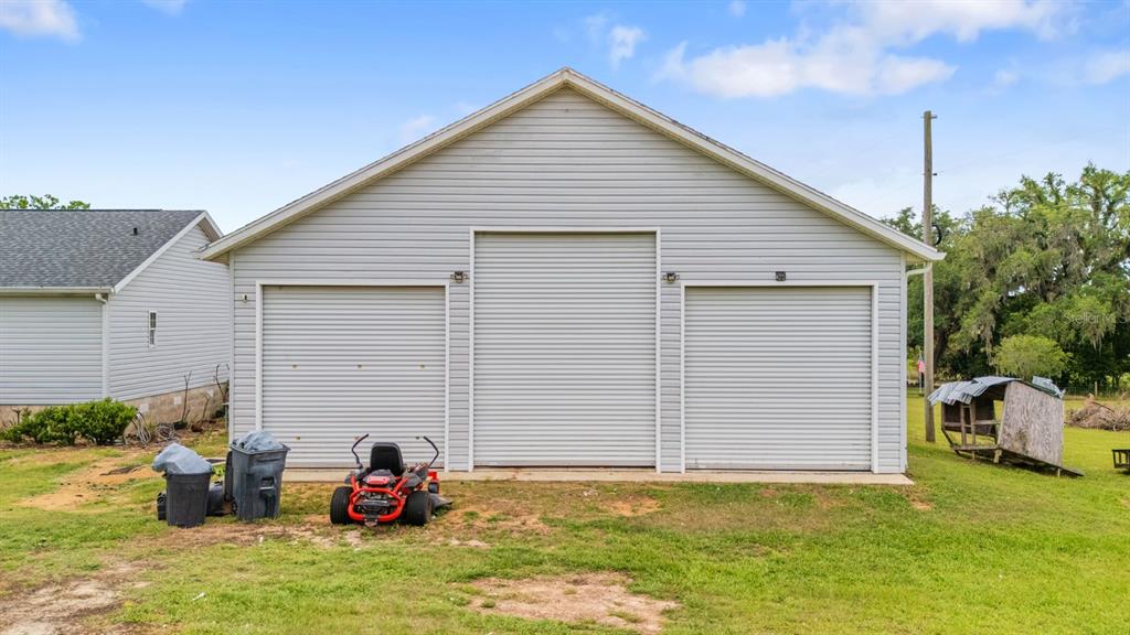 A detached garage with three roll-up doors sits on a grassy lot — 37520 PHELPS ROAD, ZEPHYRHILLS, FL