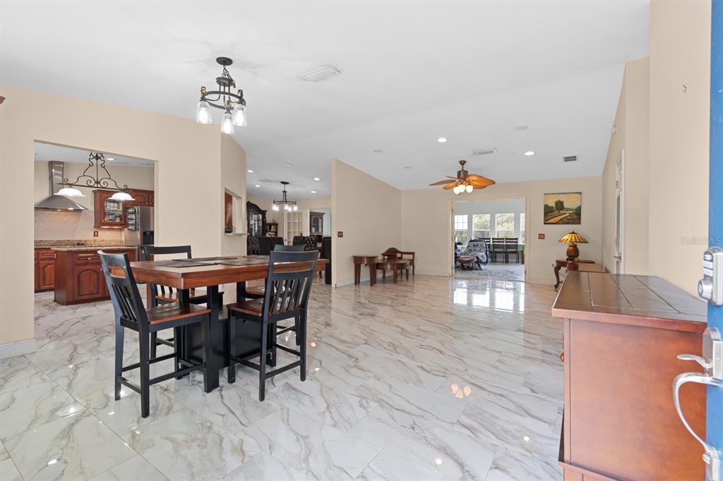 A dining area with a wooden table and chairs sits on white marble-look tile floors — 37520 PHELPS ROAD, ZEPHYRHILLS, FL