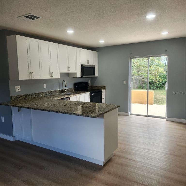 A kitchen with white cabinets, granite countertops, and a sliding glass door leading outside — 12230 SKYLER LANE, SPRING HILL, FL