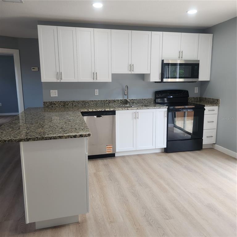 A kitchen features white cabinets, granite countertops, stainless steel appliances, and light wood-look flooring — 12230 SKYLER LANE, SPRING HILL, FL