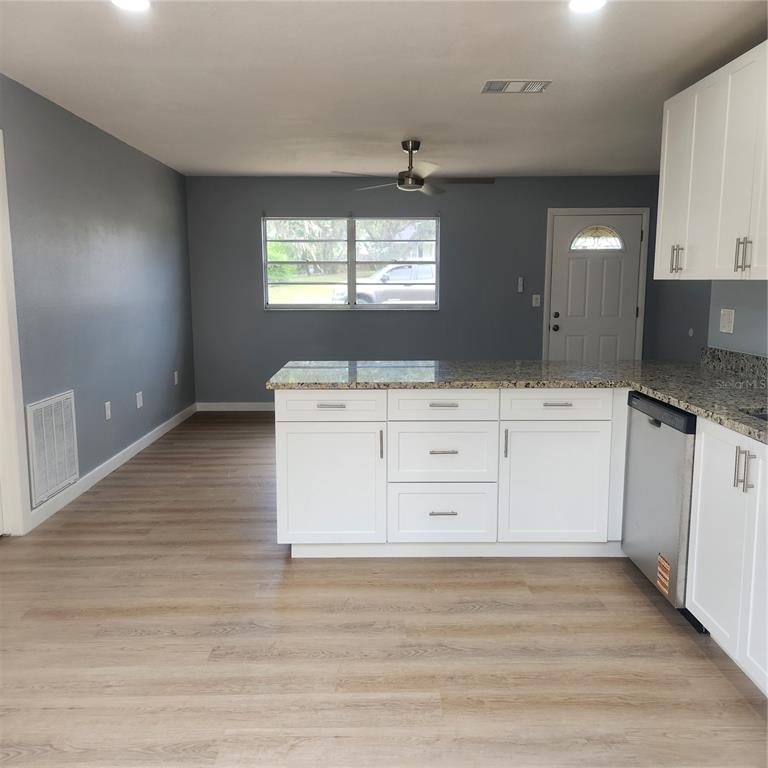 A kitchen with white cabinets, granite countertops, and light wood-look flooring opens to a living area — 12230 SKYLER LANE, SPRING HILL, FL