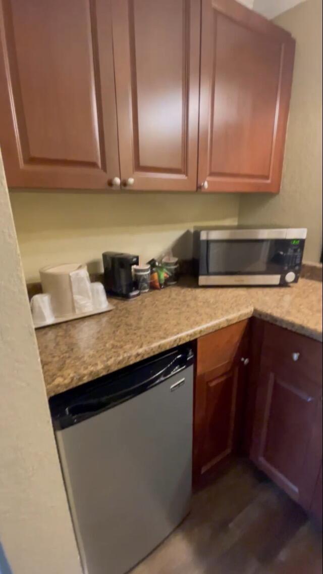A small kitchenette features wood cabinets, a microwave, and a compact refrigerator on granite countertops — 2555 9th Street N # 152, Naples FL 34103, NAPLES, FL