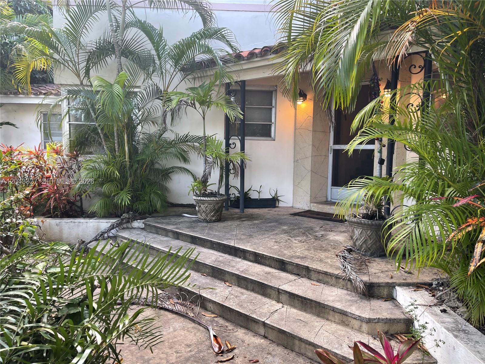 A concrete porch with steps leads to the front entrance of a stucco house — CORAL GABLES, FL