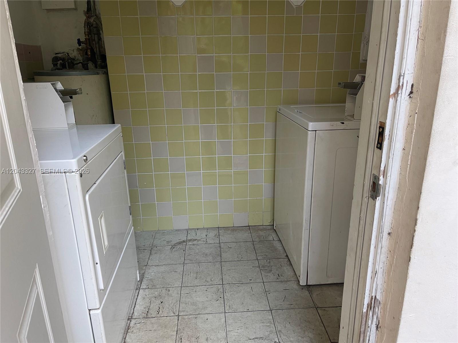 A laundry room features a washer, dryer, yellow tiled walls, and light-colored floor tiles — CORAL GABLES, FL