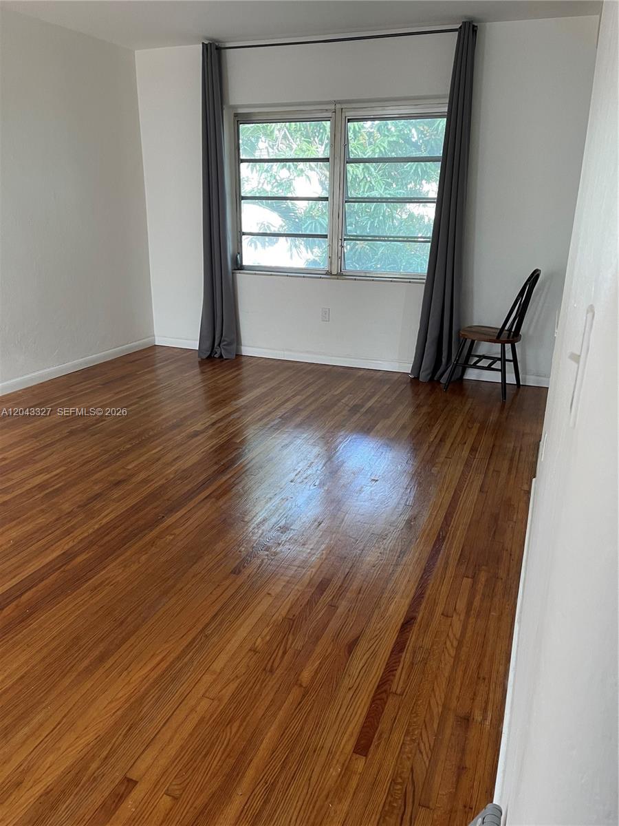 An empty room features hardwood floors, a window with gray curtains, and a wooden chair — CORAL GABLES, FL