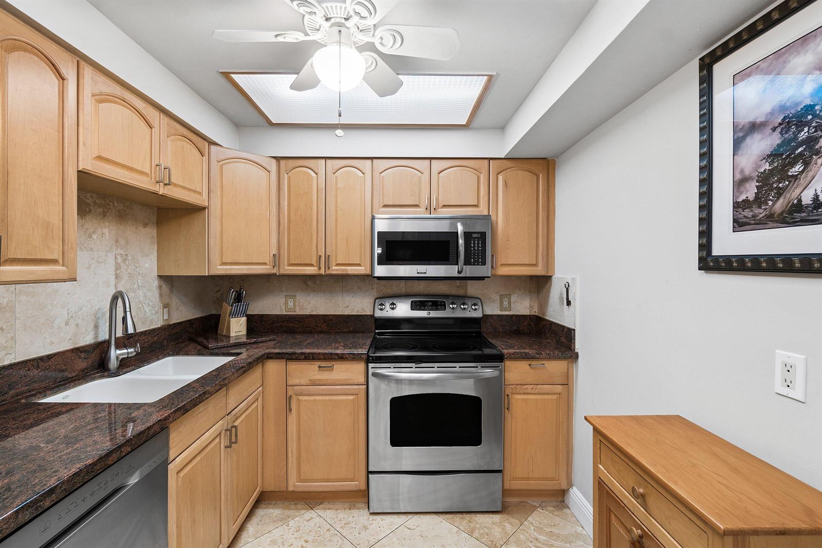 A kitchen features light wood cabinets, dark granite countertops, and stainless steel appliances — HIGHLAND BEACH, FL