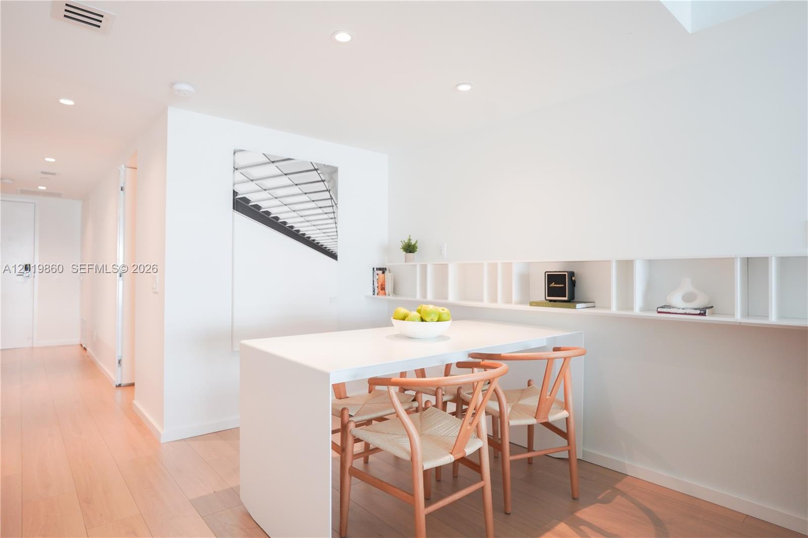 A modern dining area features a white table, wooden chairs, and built-in wall shelving — 10250 Collins Avenue # 407, Bal Harbour FL 33154, BAL HARBOUR, FL
