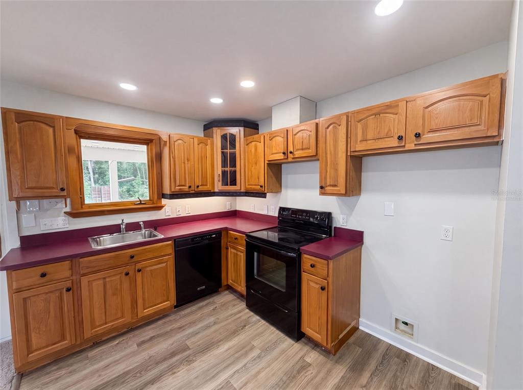 A kitchen features wood cabinets, purple countertops, black appliances, and light wood-look flooring — 9701 BLACK BEAR COURT, NEW PORT RICHEY, FL