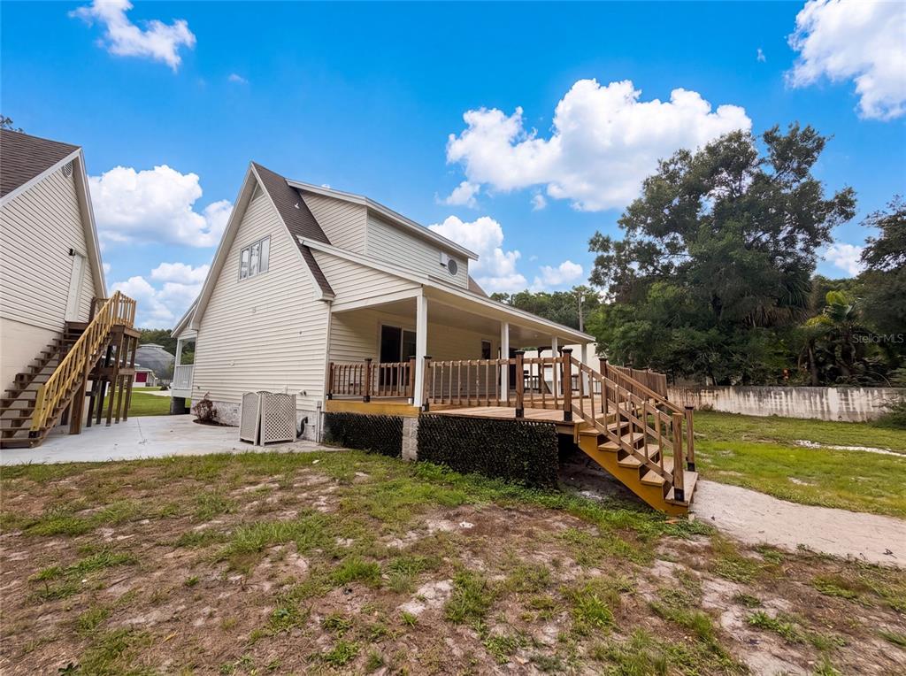 A beige two-story house features a large wooden deck with stairs and a concrete patio — 9701 BLACK BEAR COURT, NEW PORT RICHEY, FL