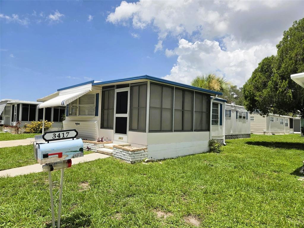 A single-story mobile home features a screened-in front porch and a mailbox in the yard — 3415 SPANISH OAK TERRACE, SARASOTA, FL
