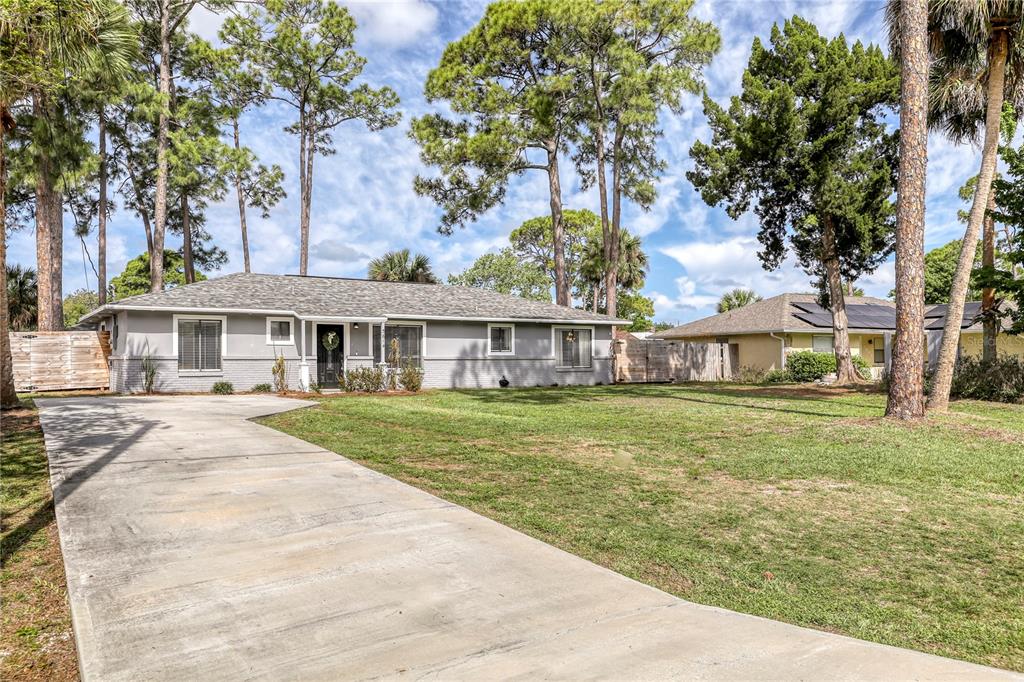 A single-story gray house with a concrete driveway and tall pine trees in the yard — 5614 JAMAICA ROAD, COCOA, FL