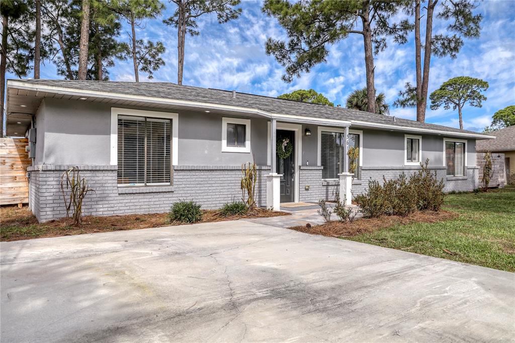 A single-story house with gray painted brick and siding features a concrete driveway and trees — 5614 JAMAICA ROAD, COCOA, FL