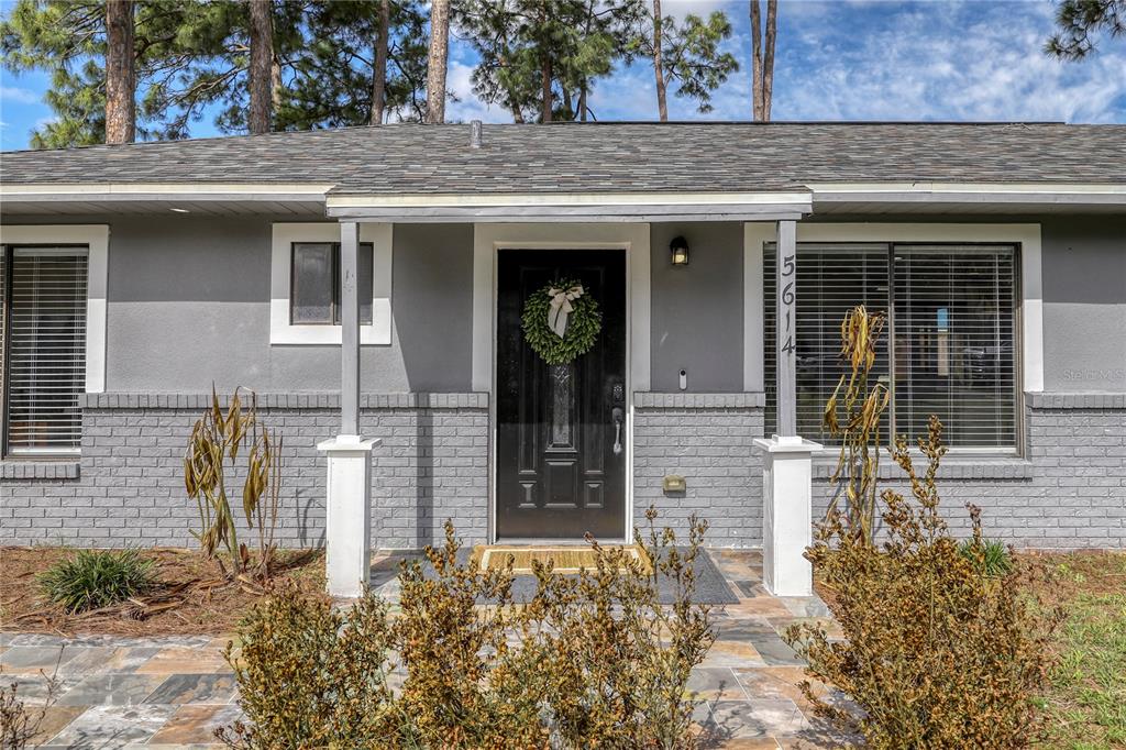The front exterior of a gray house features a black door, brick base, and windows — 5614 JAMAICA ROAD, COCOA, FL