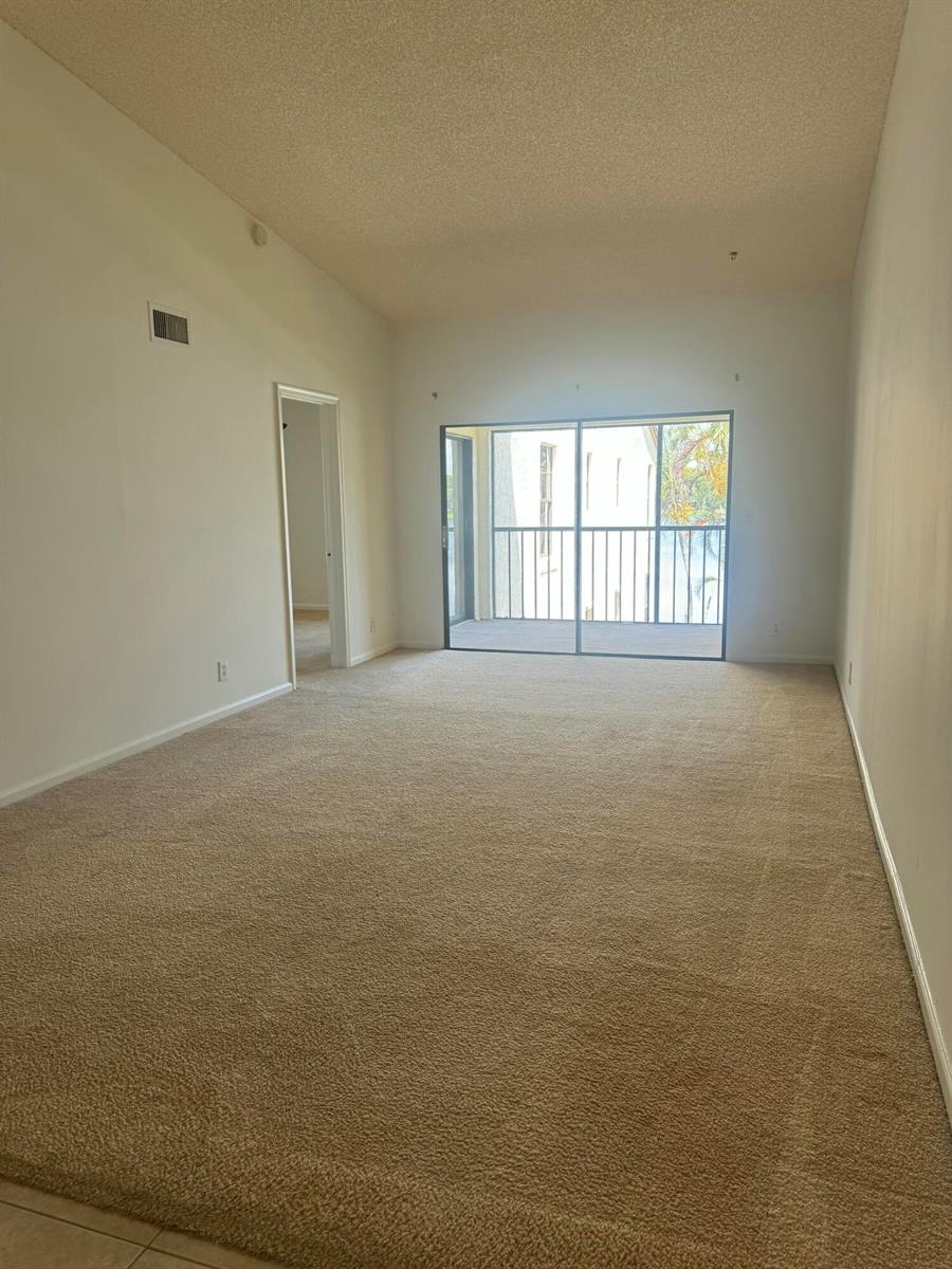 An empty living room features beige carpeting, white walls, and a sliding glass door — 2650 Greenwood # G216, Boca Raton FL 33431, BOCA RATON, FL