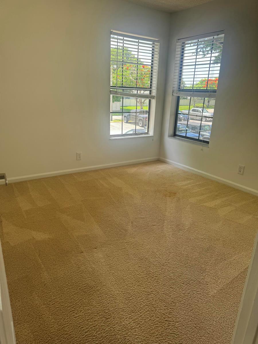 An empty bedroom with beige carpeting, white walls, and two windows overlooking a parking lot — 2650 Greenwood # G216, Boca Raton FL 33431, BOCA RATON, FL