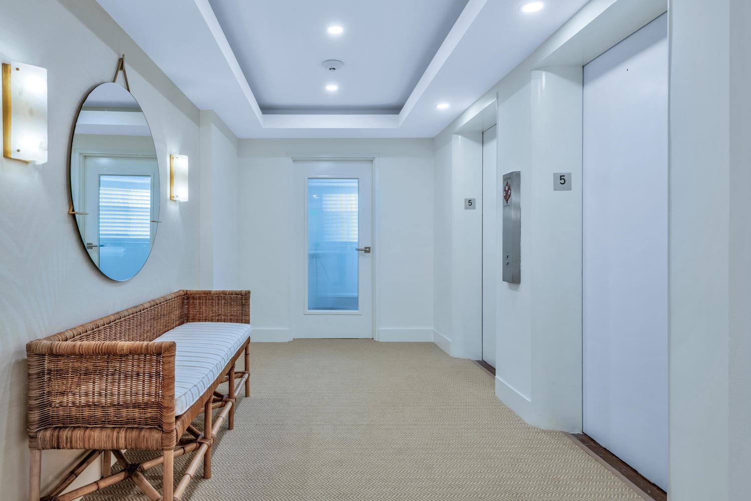 A hallway features a wicker bench, a round mirror, and two elevator doors on level five — 170 N Ocean Boulevard Boulevard # 411, Palm Beach FL 33480, PALM BEACH, FL