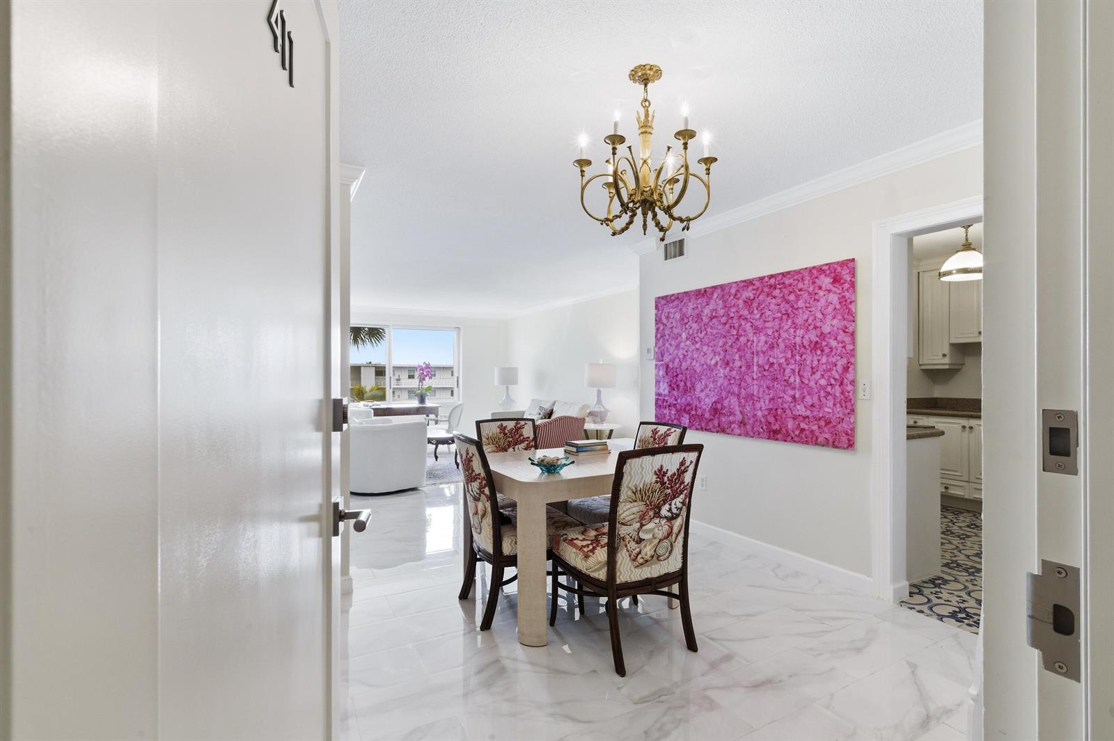 A dining area with a chandelier and patterned chairs sits next to a bright pink painting — 170 N Ocean Boulevard Boulevard # 411, Palm Beach FL 33480, PALM BEACH, FL