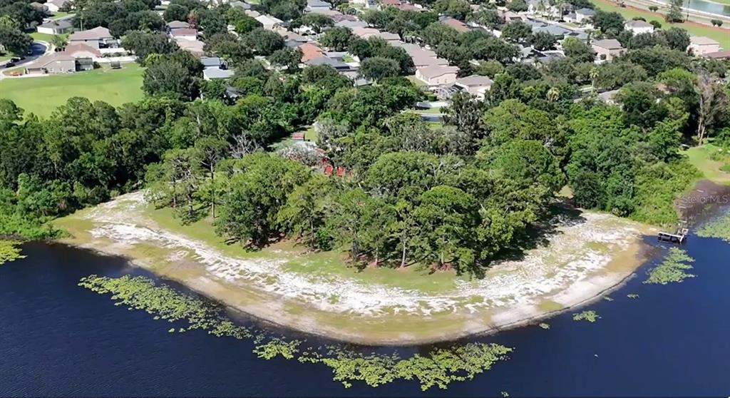 An aerial view shows a wooded lot bordering a lake with a sandy shoreline — 2636 REAGAN TRAIL, LAKE MARY, FL