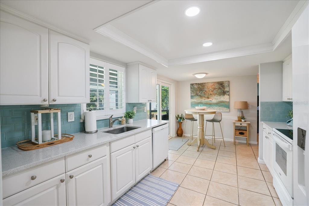 A kitchen with white cabinets, light countertops, blue subway tile backsplash, and a dining area — 1330 CAMBRIDGE DRIVE, VENICE, FL