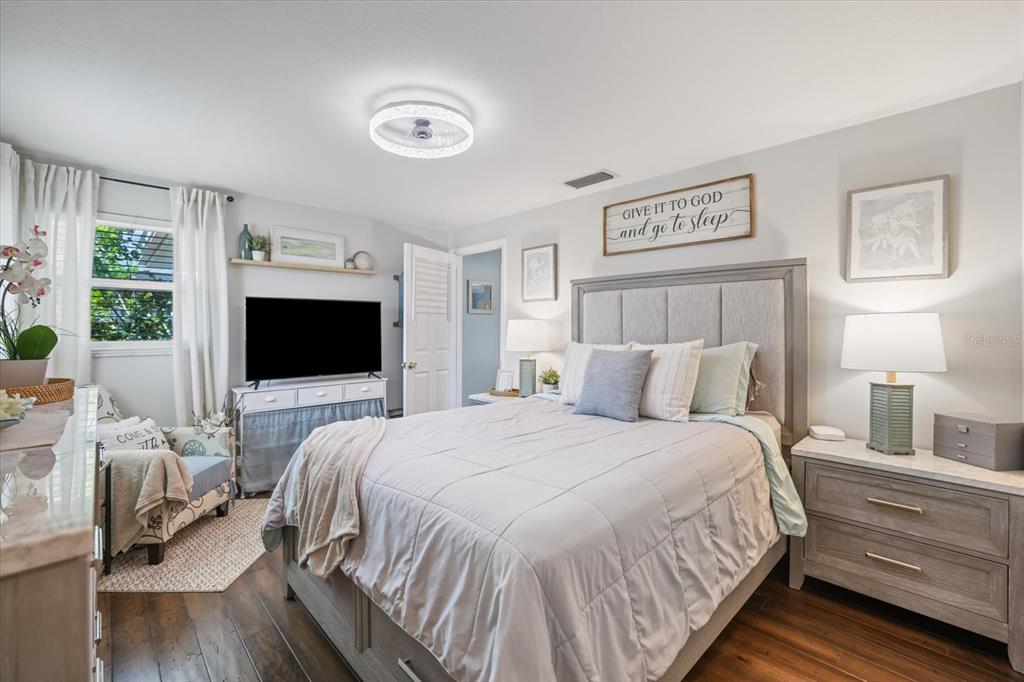 A bedroom features a gray upholstered bed, a television on a console, and wood flooring — 1330 CAMBRIDGE DRIVE, VENICE, FL