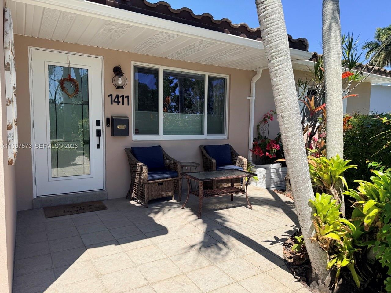 A paved front patio features two wicker chairs, a small table, and a white door — 1411 Harding St, Hollywood FL 33020, HOLLYWOOD, FL