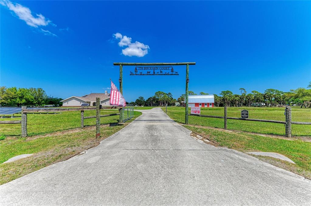 A concrete driveway leads through a wooden gate entrance toward a house and barn — 770 BUCKSKIN COURT, ENGLEWOOD, FL