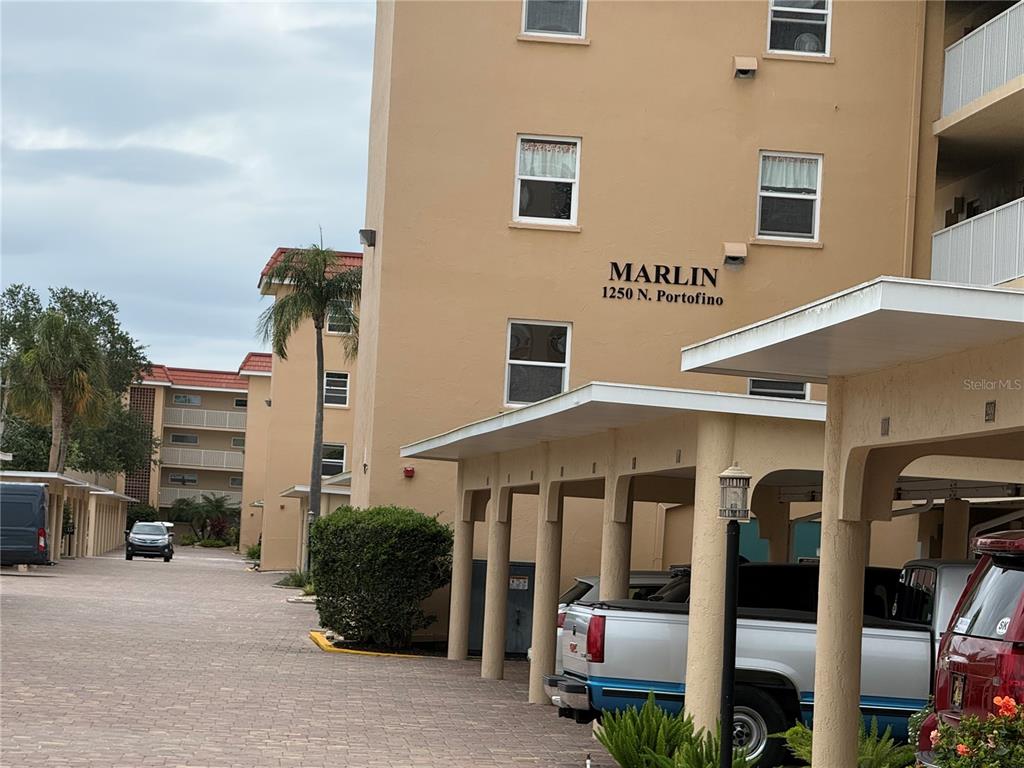 The exterior of a multi-story apartment building features covered parking and a paved driveway — 1250 N PORTOFINO DRIVE UNIT 202, SARASOTA, FL